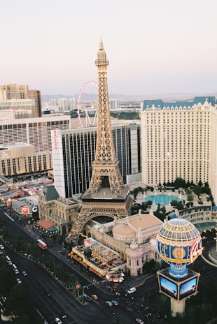 An urban landscape featuring a detailed replica of the Eiffel Tower surrounded by high-rise buildings, bustling streets, and a distinctive blue and golden globe structure. The scene captures the essence of a vibrant city with numerous hotels and casinos, indicative of a popular tourist destination.