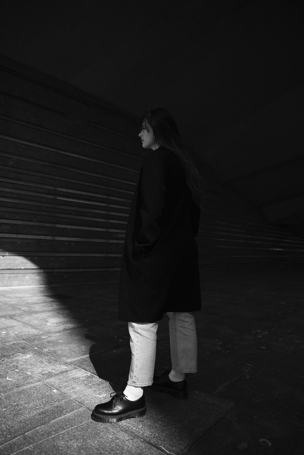 woman in black coat and white pants standing on the sidewalk