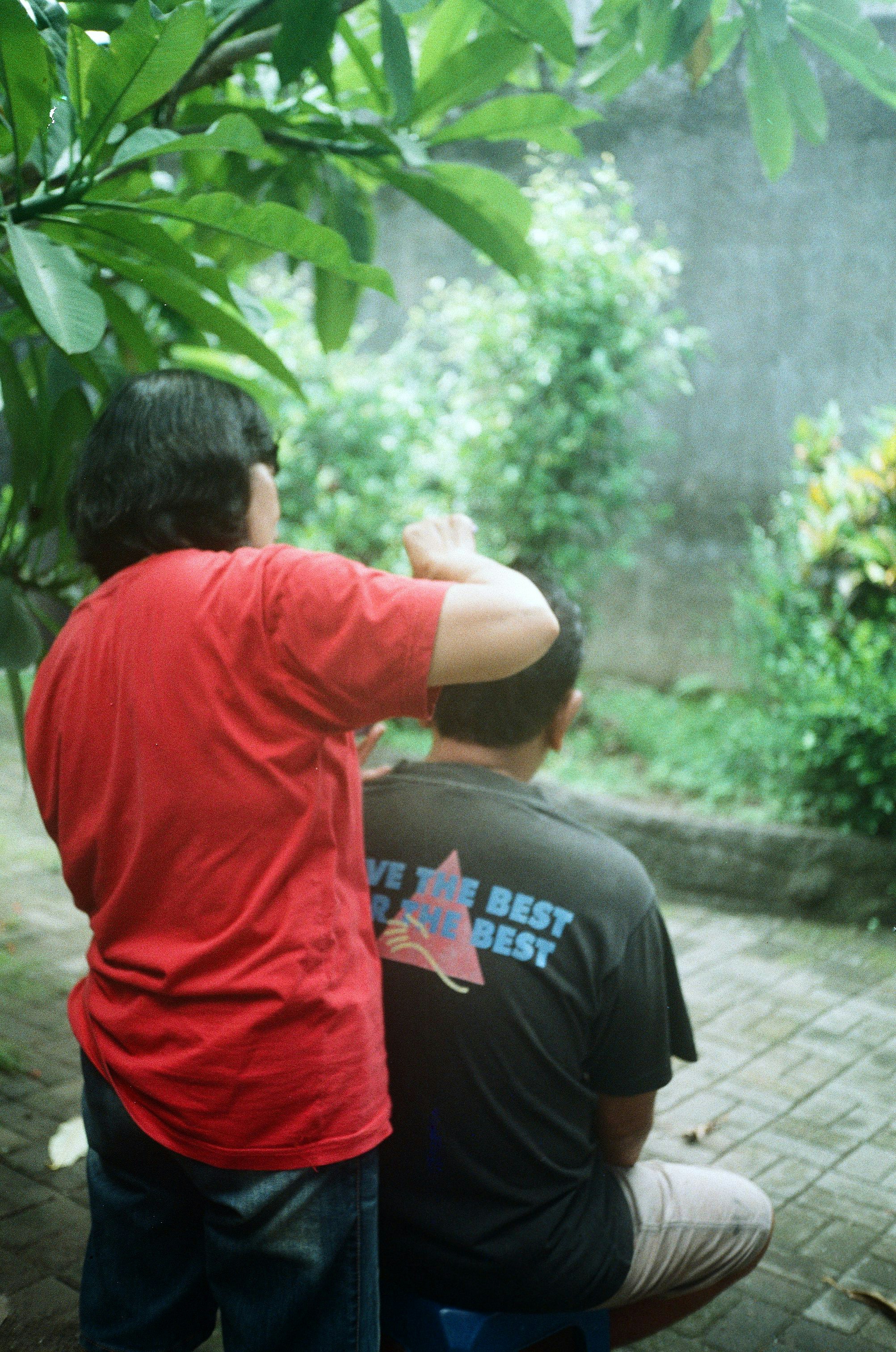 man in red crew neck t-shirt standing near green leaf plant during daytime