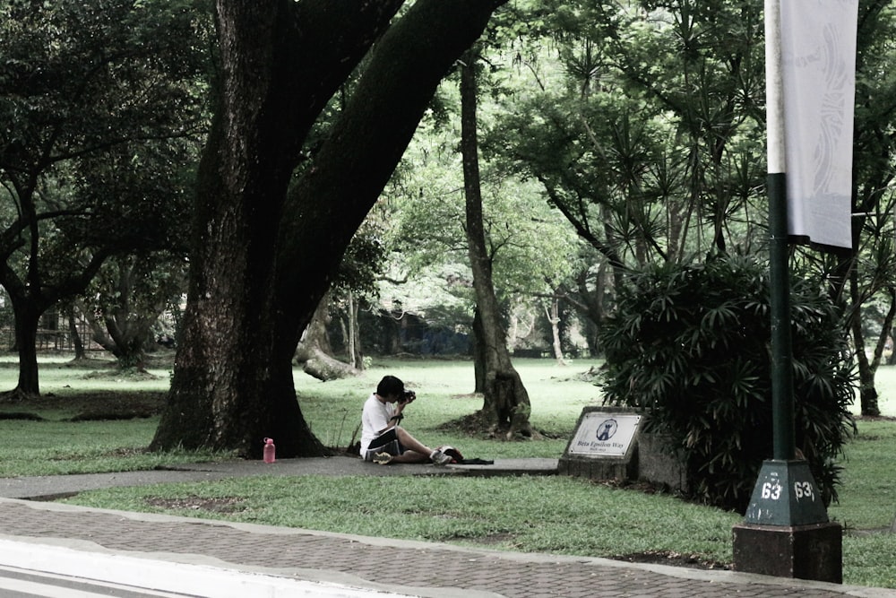 Mann im weißen T-Shirt sitzt tagsüber auf einer braunen Holzbank unter grünen Bäumen