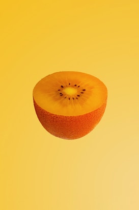 A halved kiwifruit with a rich golden yellow interior and small black seeds is centered against a matching yellow background. The even lighting and smooth gradient enhance the vibrant color and texture of the fruit.