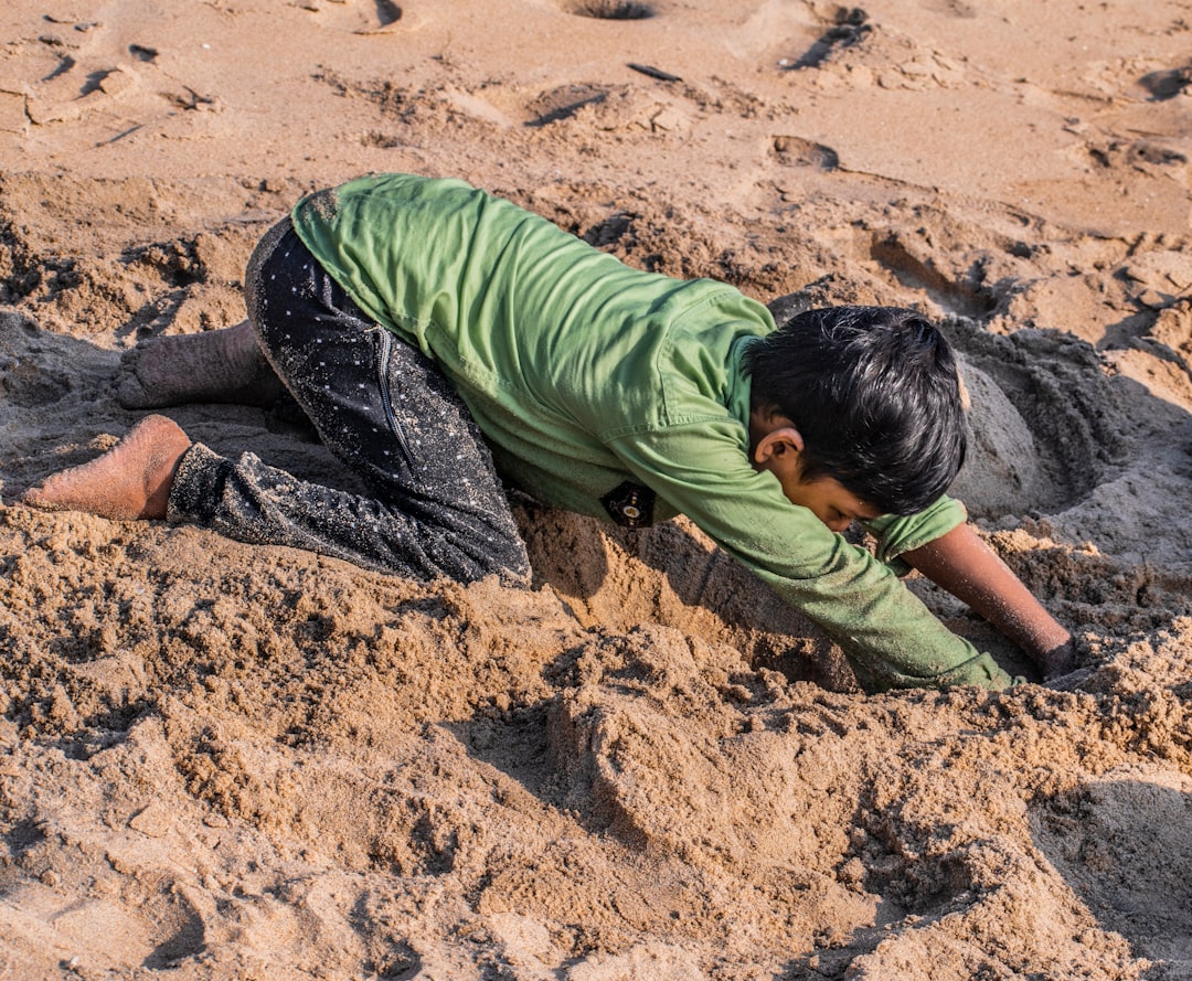 man in green shirt and black pants sitting on brown sand during daytime