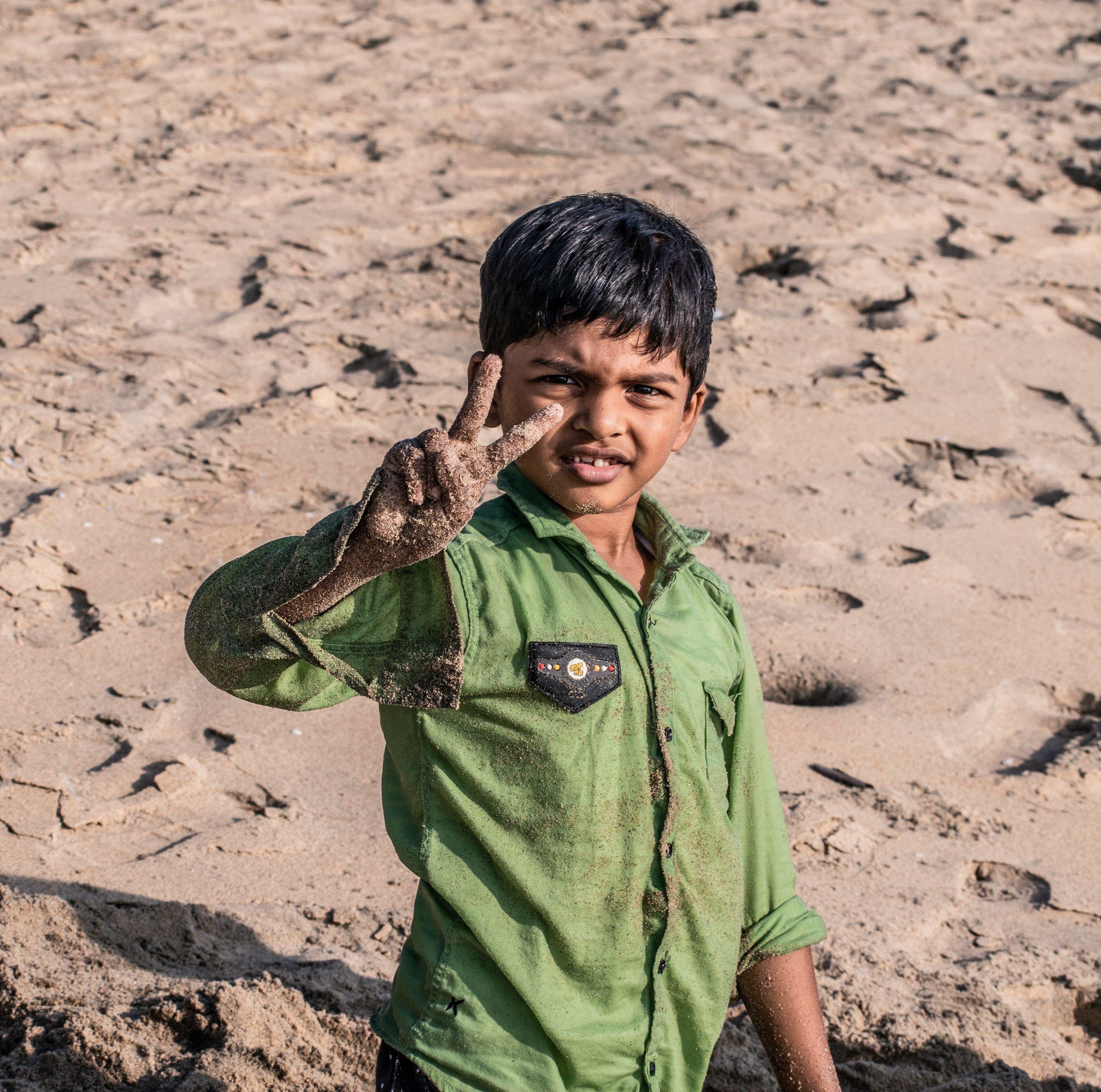 boy in green polo shirt holding brown and black snake on brown sand during daytime
