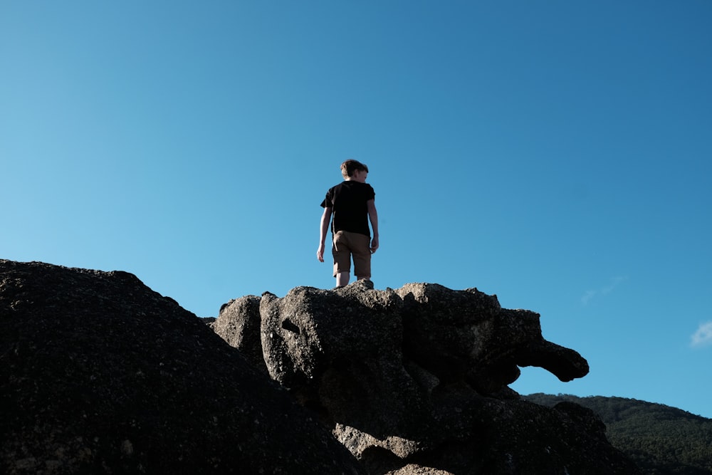 Hombre con camisa negra de pie en una formación rocosa bajo el cielo azul durante el día