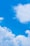 A clear blue sky with a commercial airplane soaring above fluffy white clouds.
