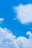 A clear blue sky with a commercial airplane soaring above fluffy white clouds.