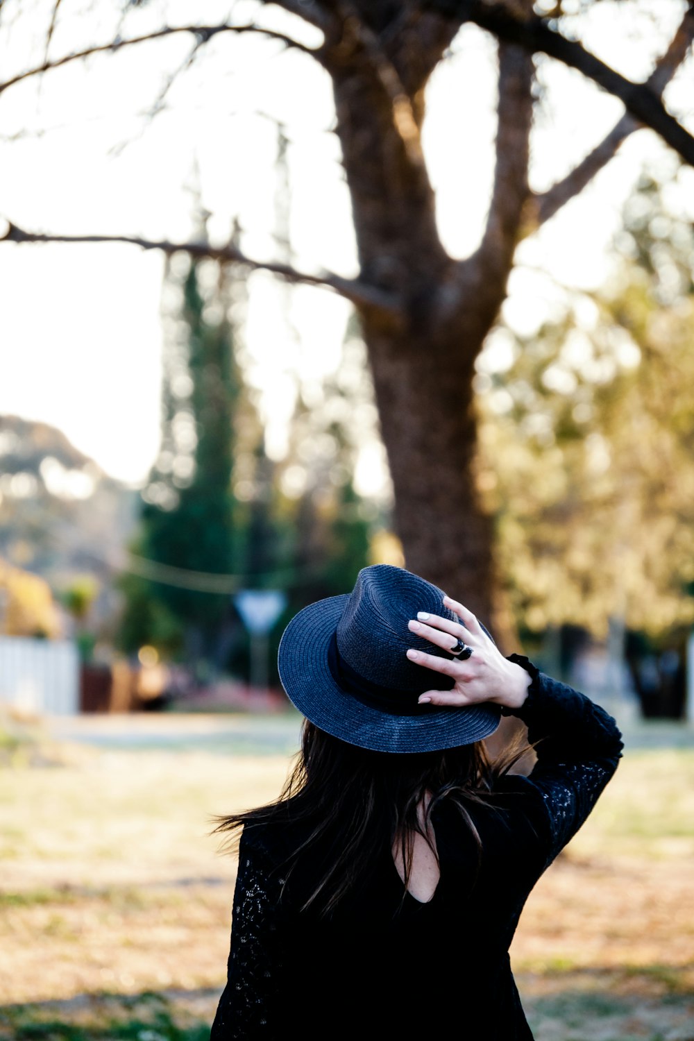 昼間、木のそばに立つ青い帽子と黒い長袖シャツを着た女性