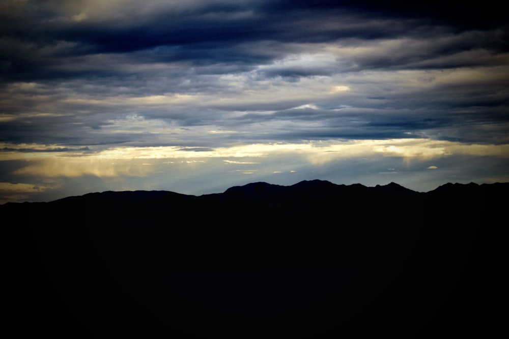 silhouette of mountains under cloudy sky during sunset