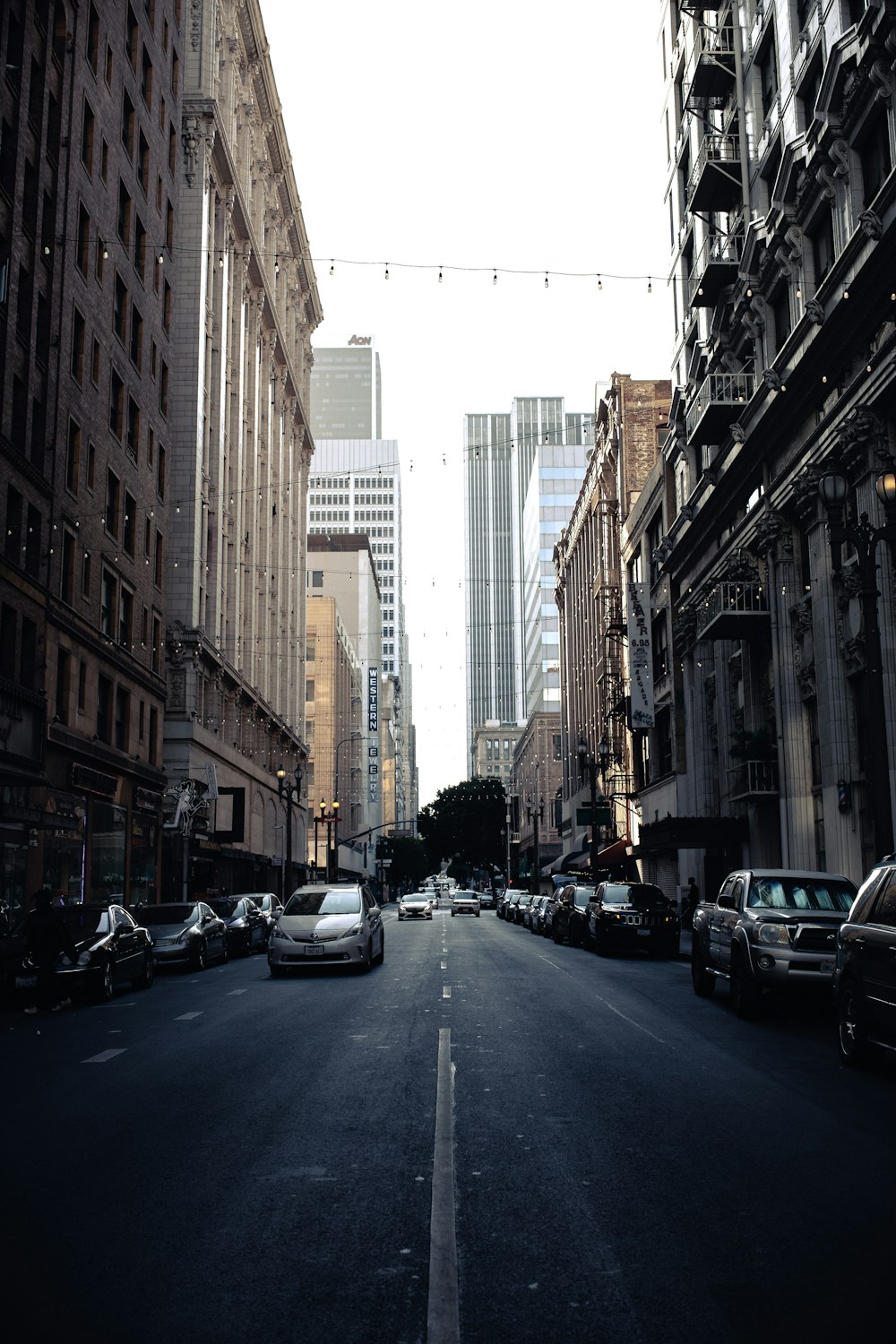 cars parked on side of the road in between high rise buildings during daytime