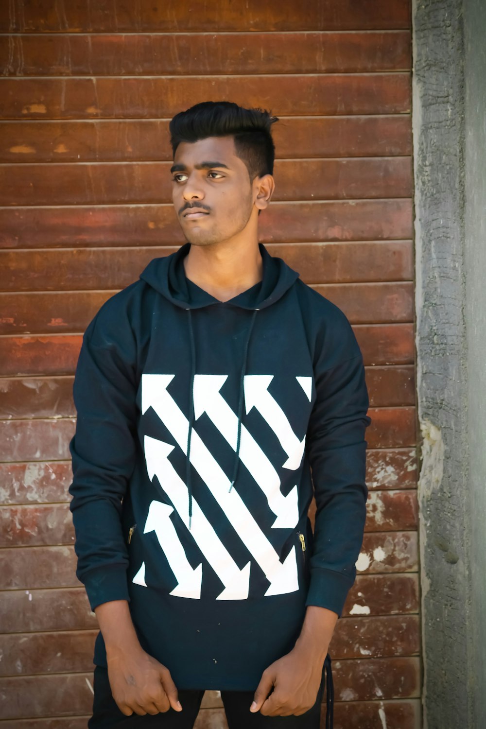 man in black and white adidas hoodie standing beside brown brick wall