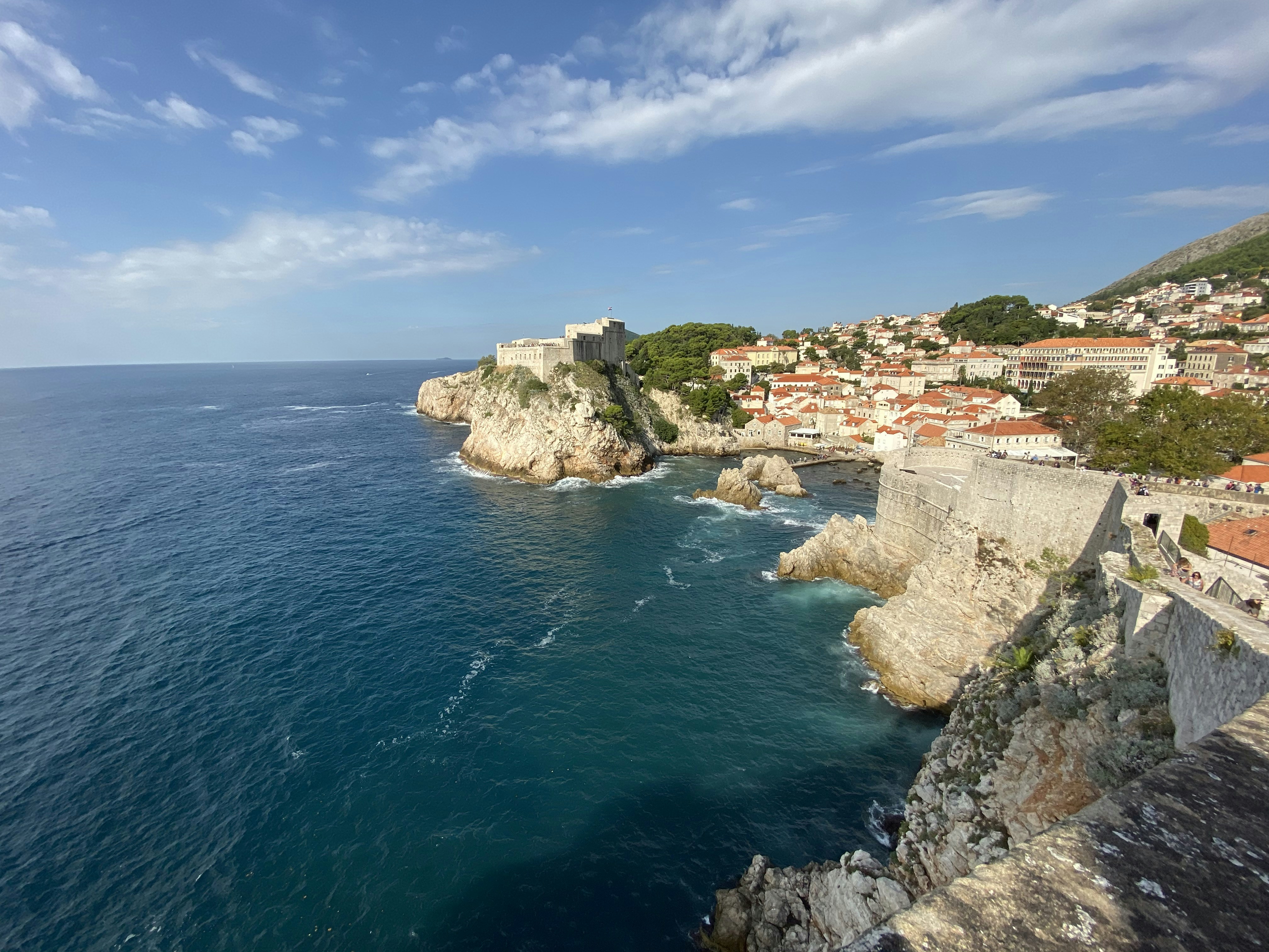 Houses on cliff by the sea under blue and white cloudy sky during daytime
