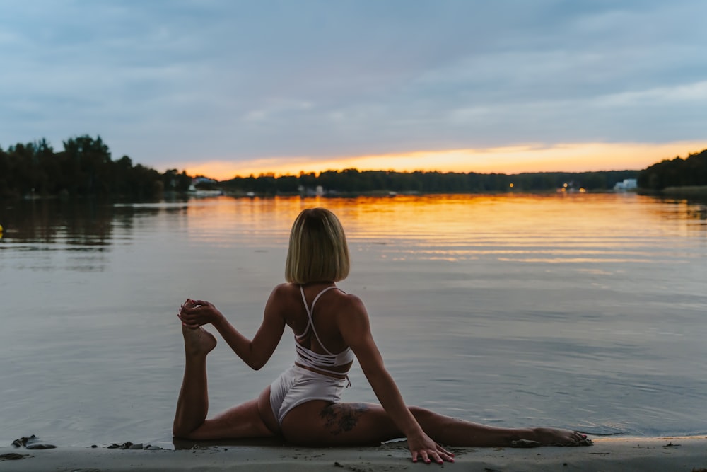 woman in white tank top sitting on the beach during sunset