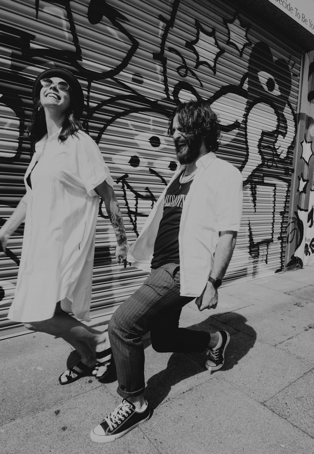 grayscale photo of man and woman walking on sidewalk