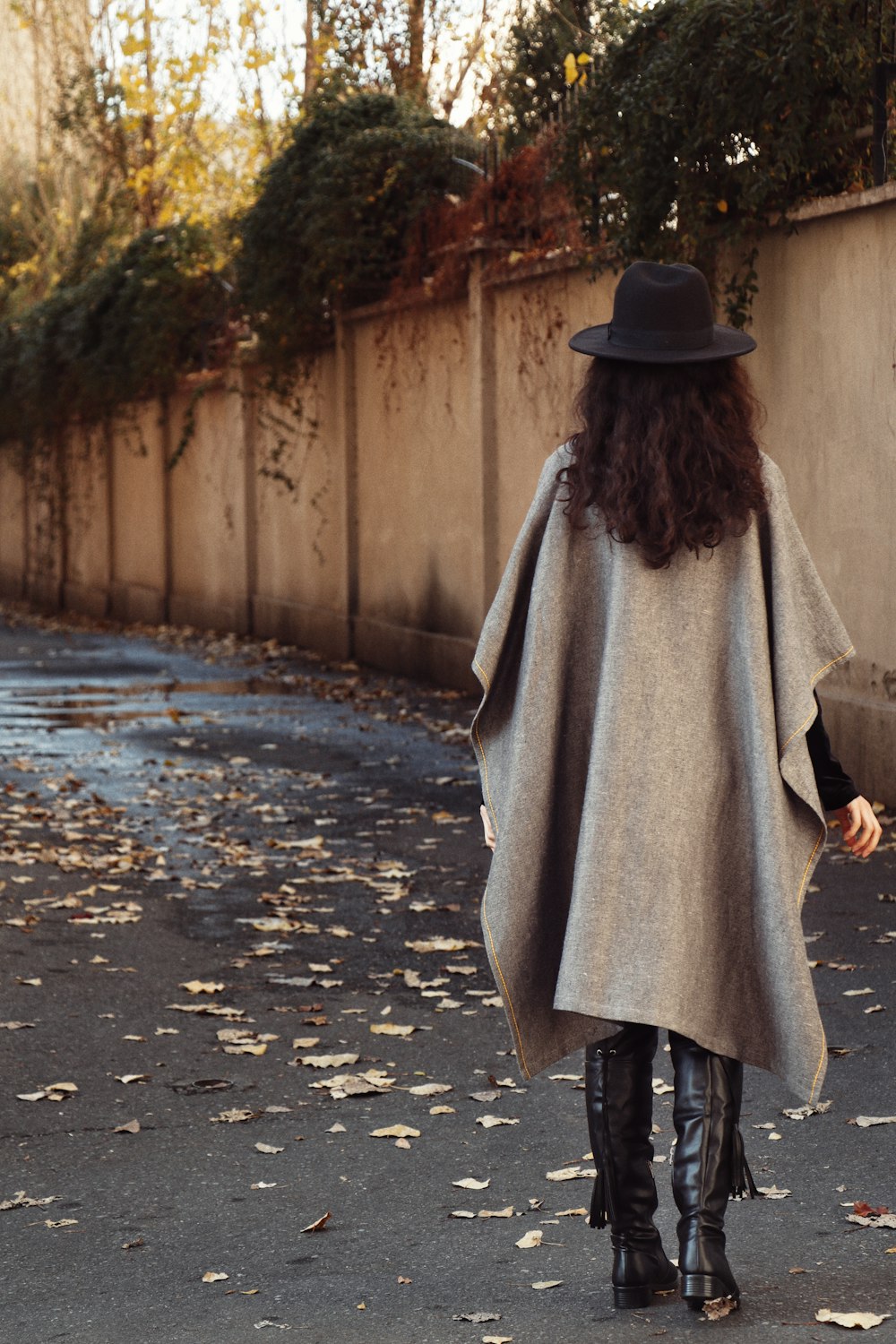 woman in black hat and gray coat walking on street during daytime