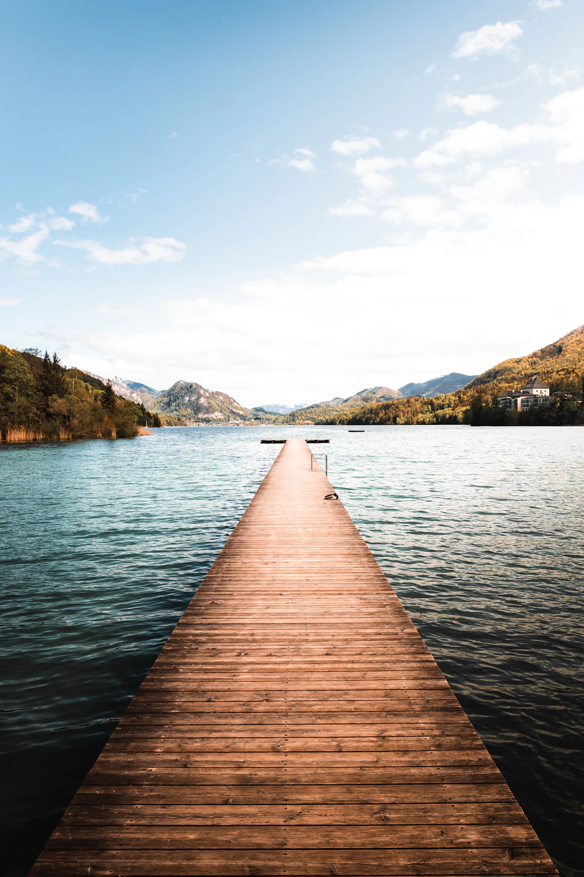 A long wooden jetty running out into Fuschlsee, with green hills and a few houses on the shore