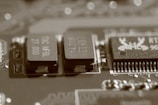 A close-up view of an electronic circuit board, featuring several visible electronic components such as integrated circuits and capacitors. The image has a sepia tone, giving it a vintage appearance, and the components are detailed with numbers and letters etched on their surfaces.