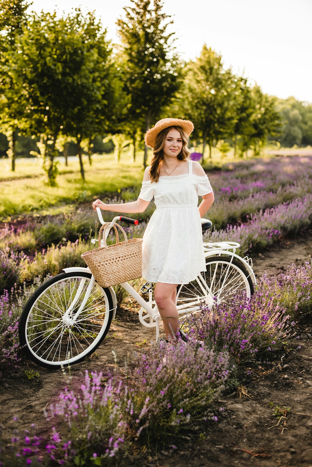 woman in white dress and brown hat standing on purple flower field during daytime