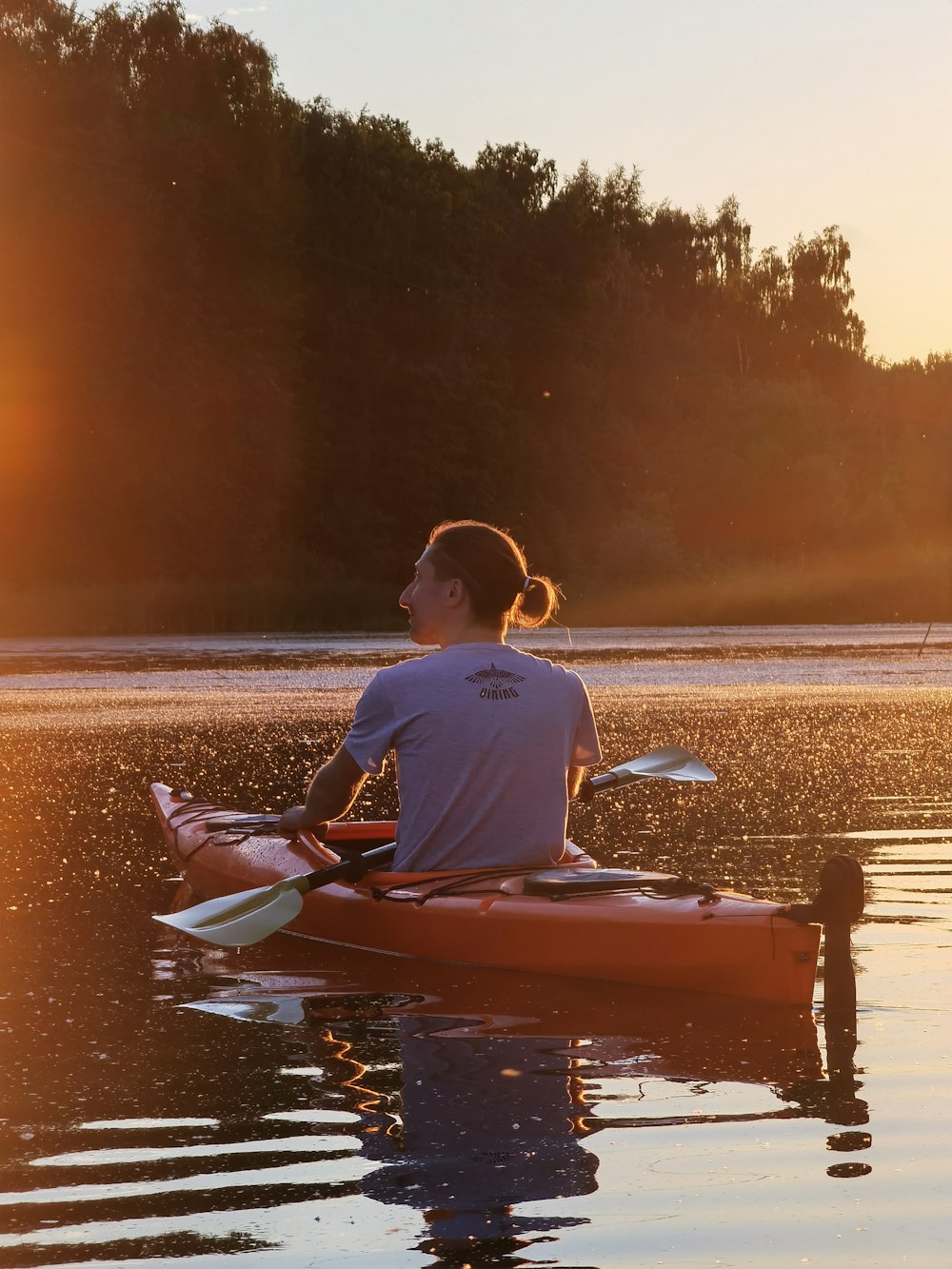 man in blue shirt riding red kayak on sea shore during sunset