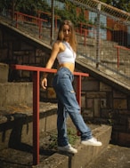 a woman in a white top and jeans leaning on a rail