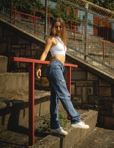 a woman in a white top and jeans leaning on a rail