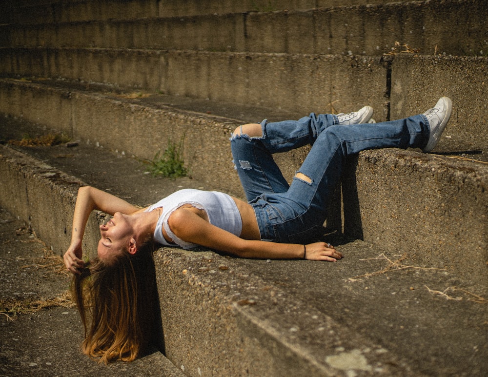 Mujer con camiseta blanca sin mangas y jeans de mezclilla azules acostada en el piso de concreto