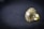 A close-up of a gold-toned earring with a central diamond surrounded by smaller gemstones, resting on a dark textured surface. The intricate design is highlighted by the shiny metal and transparent stones, creating a luxurious and elegant appearance.