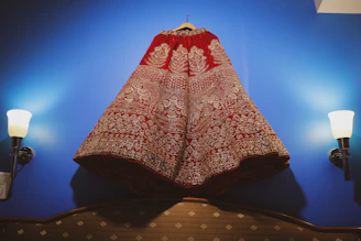 A close-up of a delicate gold-embroidered dark green children's dress hanging softly on a wooden hanger.