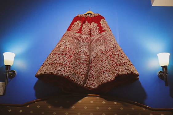 A close-up of a delicate gold-embroidered dark green children's dress hanging softly on a wooden hanger.