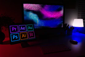 A computer monitor and tablet displaying creative software icons in a dimly lit workspace