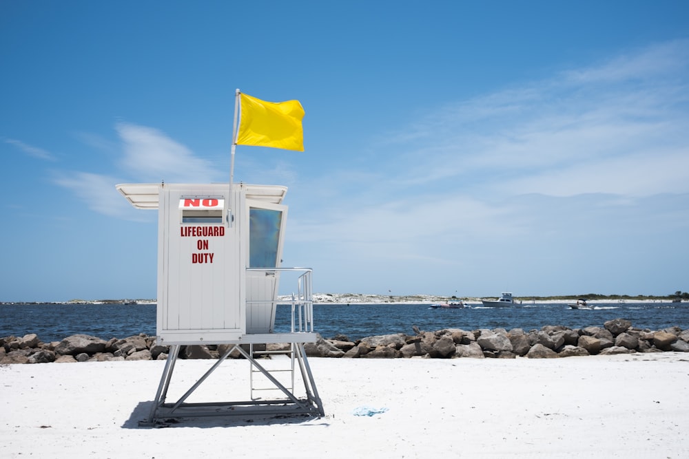 낮 동안 해변 해안에 있는 흰색 목조 인명 구조대 타워에 노란색 깃발