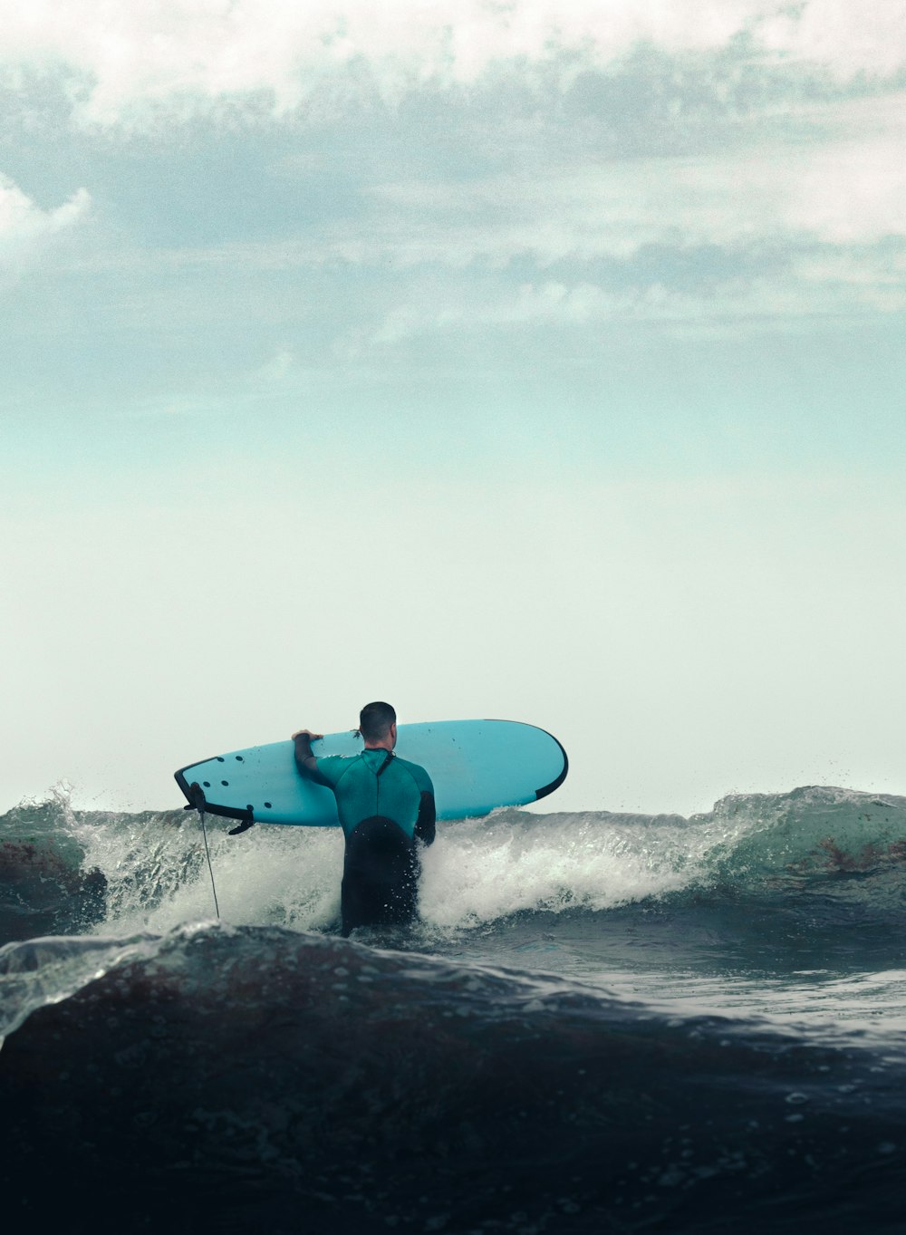 man in blue wetsuit holding blue surfboard on seashore during daytime