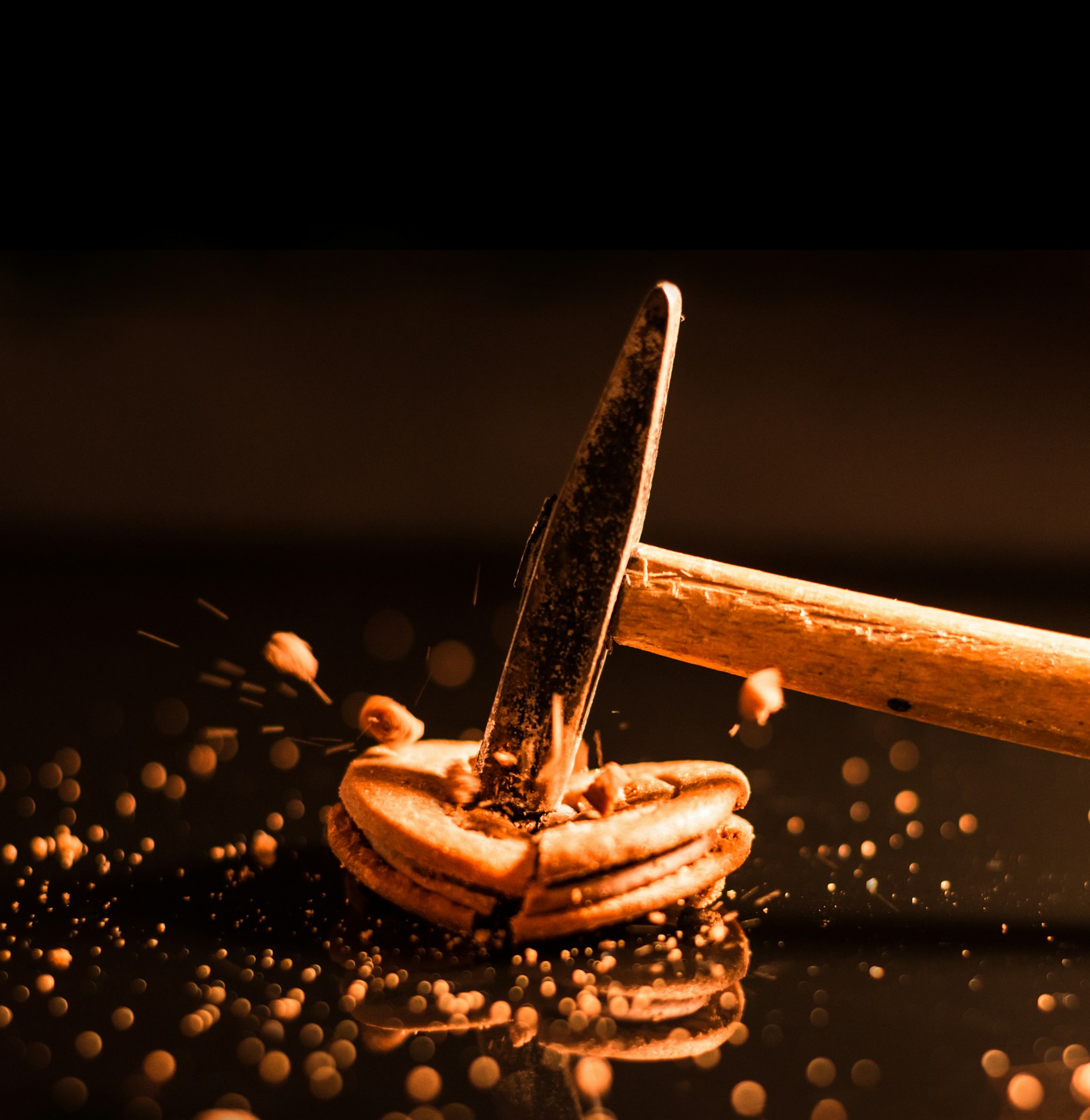 A hammer striking a nut, causing the nut to crack open with debris flying in all directions. The image is detailed with a sharp focus on the action and particles scattering around. The background is dark, directing attention to the central action.