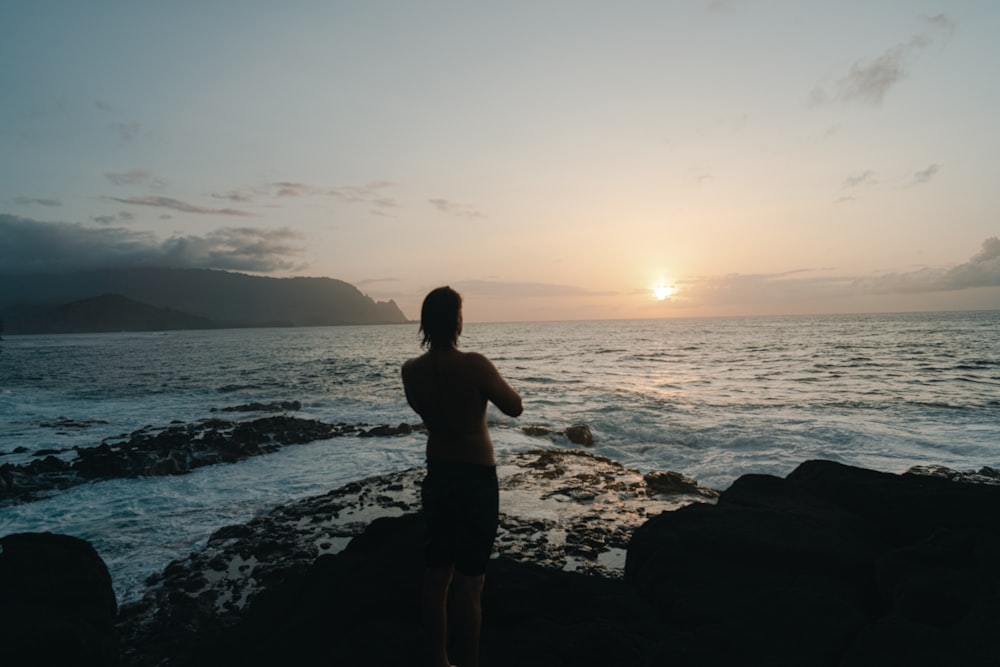 man standing on rocky shore during sunset