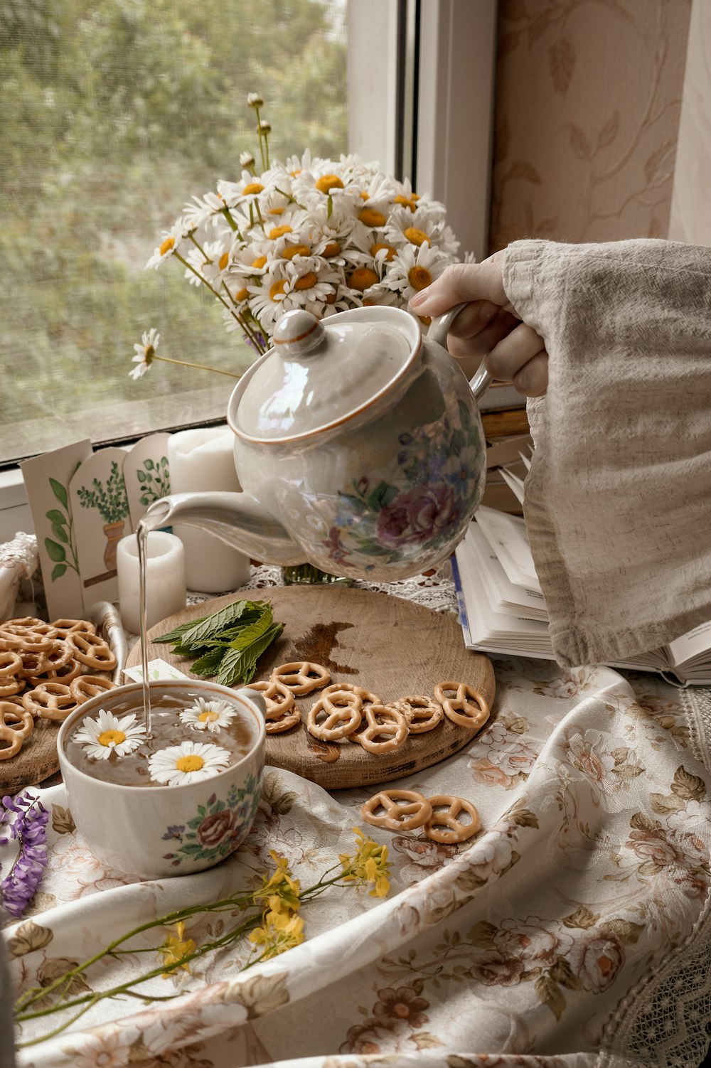 personne tenant une théière en céramique blanche versant un liquide blanc sur une tasse à thé en céramique blanche