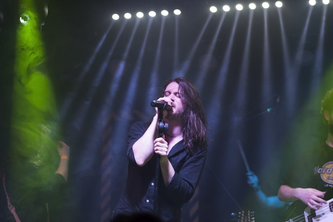 Close-up of the lead vocalist screaming into the mic, sweat glistening under green stage lights.