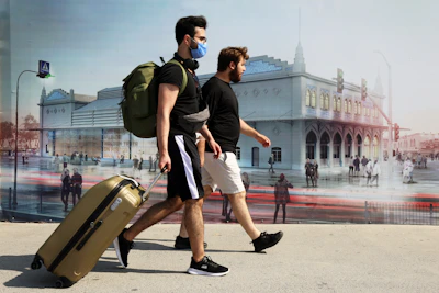 man in black t-shirt and white shorts carrying brown luggage bag walking on street during