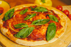 Fresh basil leaves scattered over a vibrant tomato sauce base on a pizza.