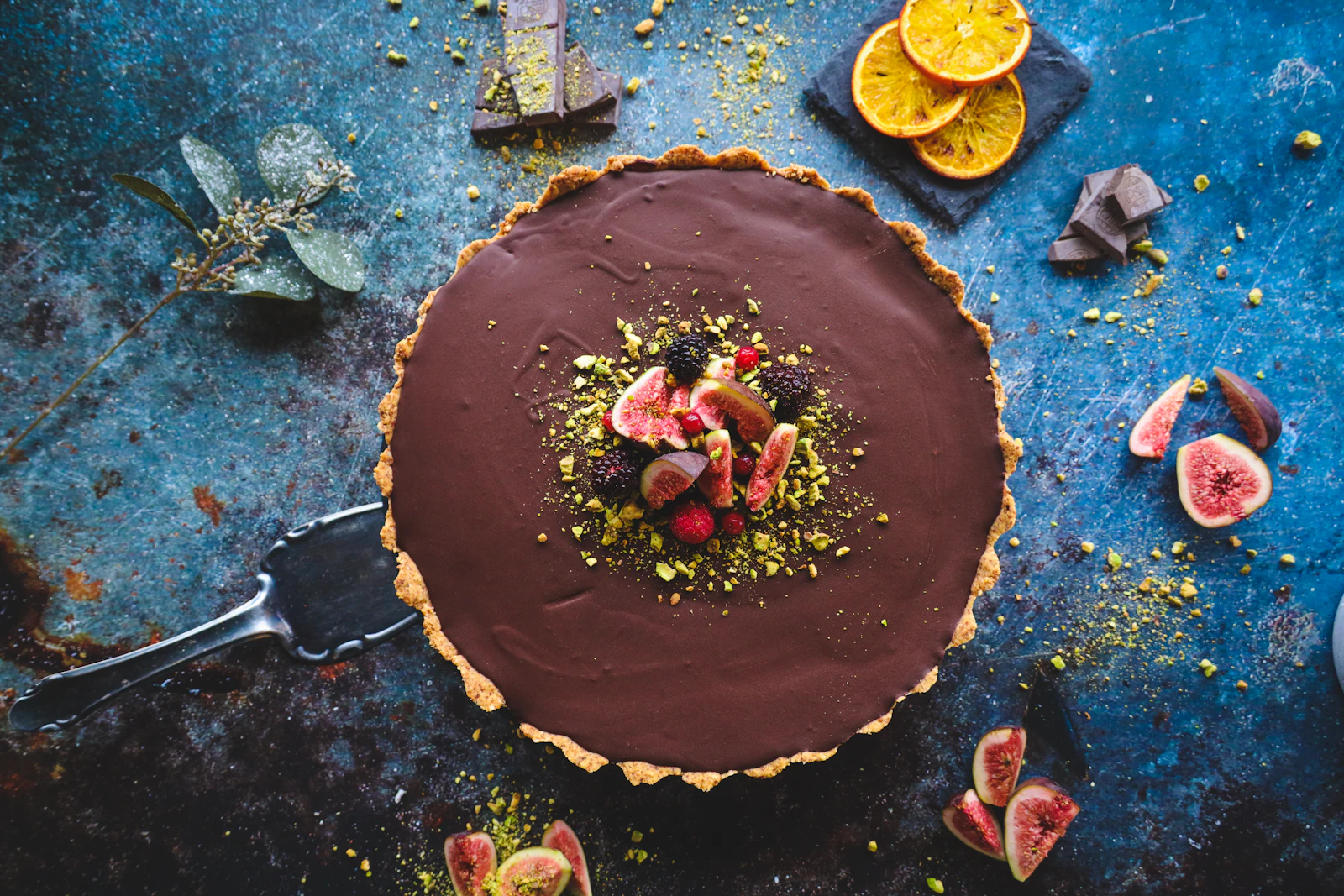 A glazed chocolate tart topped with pistachios, berries and fresh figs, photographed from above