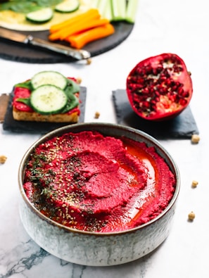 A bowl of hummus garnished with vibrant pomegranate beets and a sprinkle of Arabic dakka.