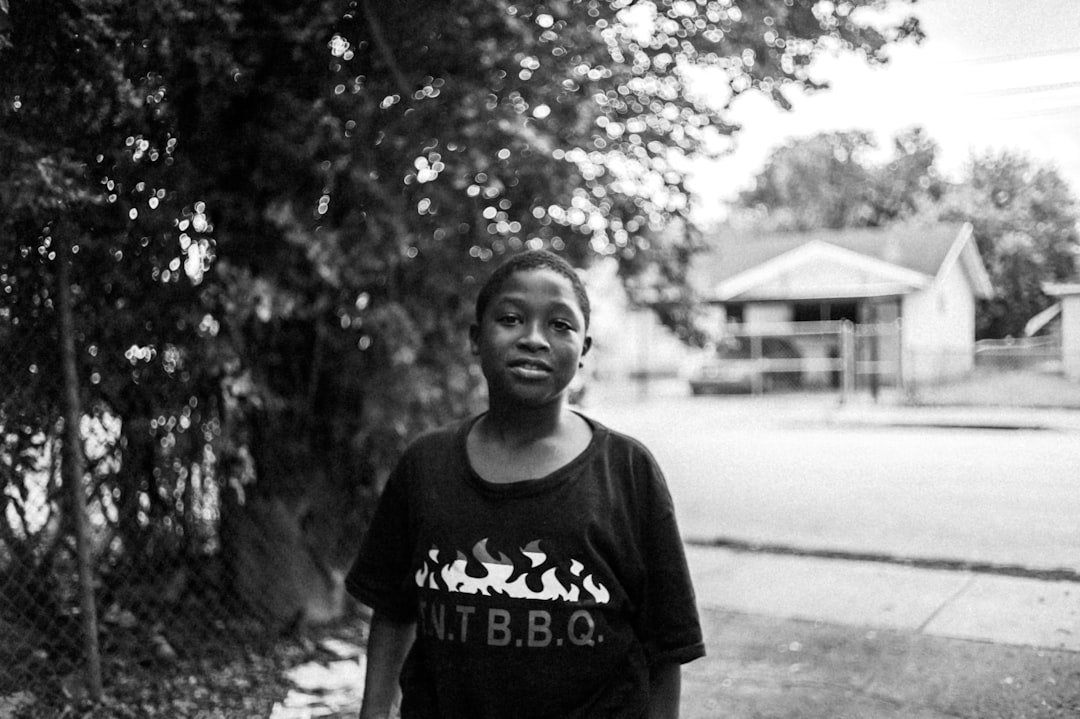 grayscale photo of boy in crew neck t-shirt standing on road