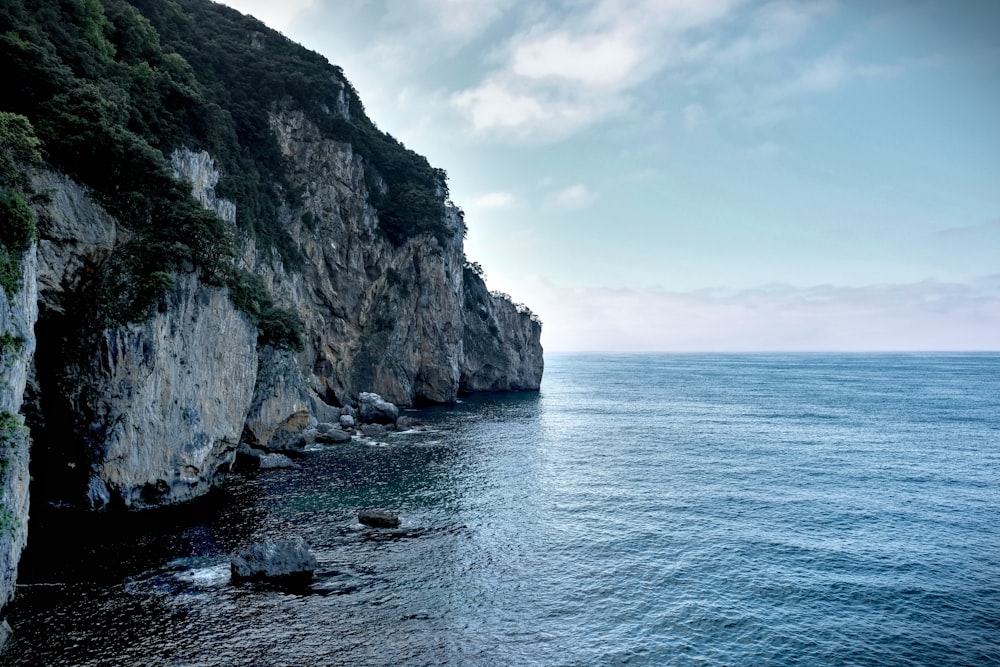 gray rocky mountain beside body of water during daytime