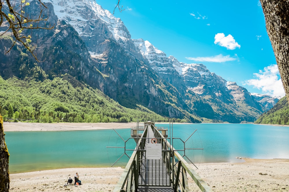 brown wooden bridge on lake near mountain range