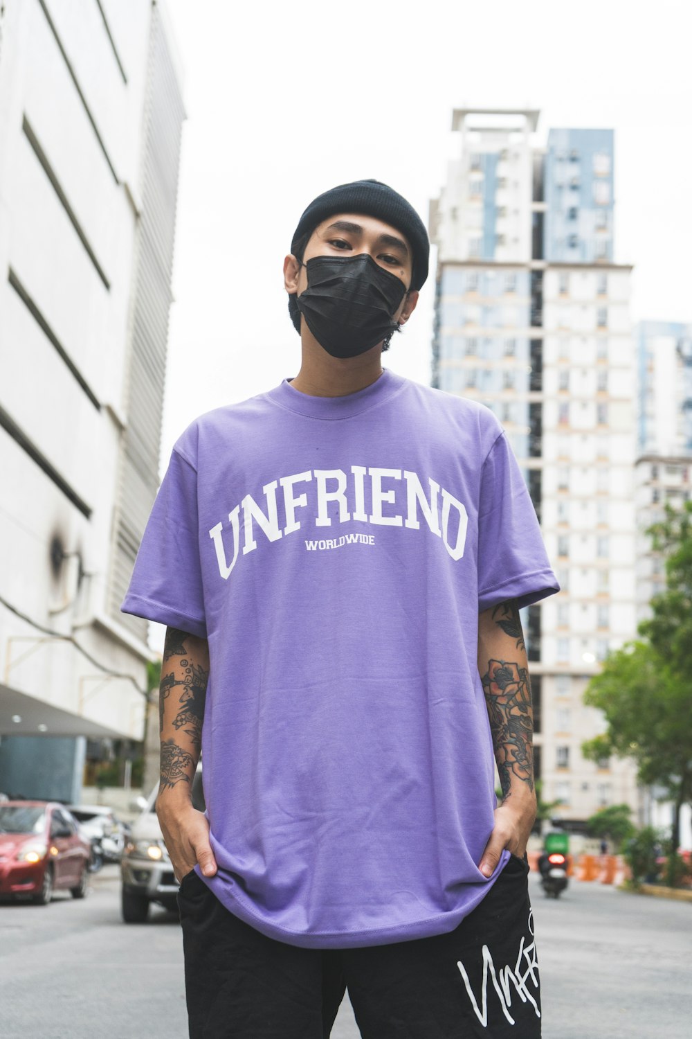 man in purple crew neck t-shirt wearing black sunglasses standing near white concrete building during