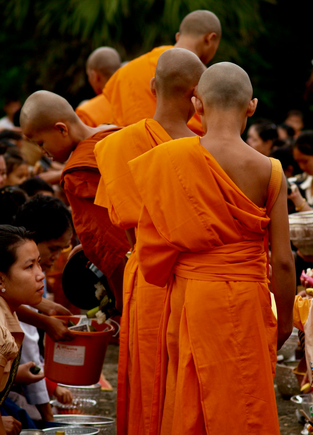 man in orange robe standing in front of people during daytime