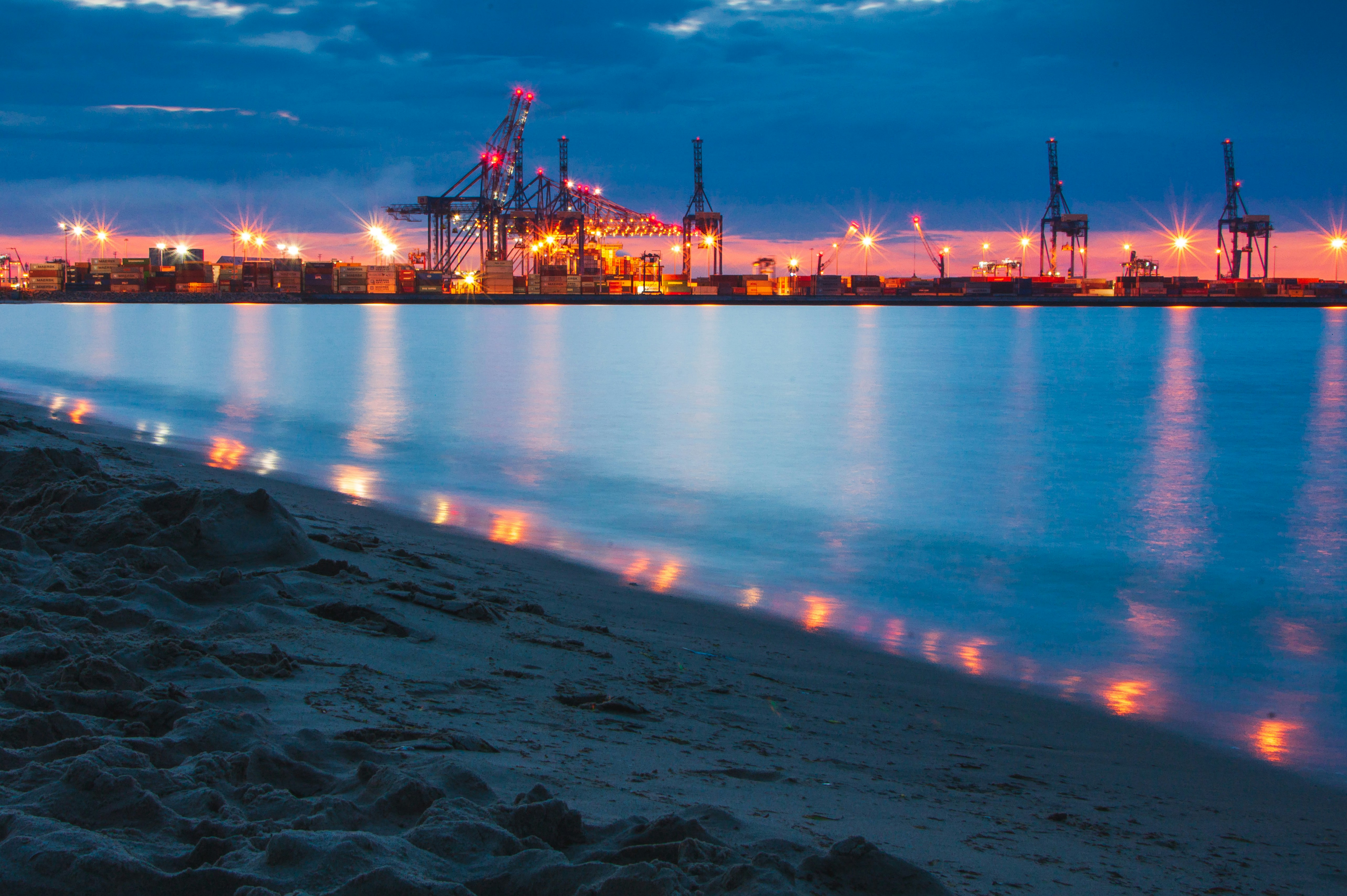 Busy Lagos port container terminal at dusk, rows of shipping containers in shadow, dim port lighting, dark industrial atmosphere