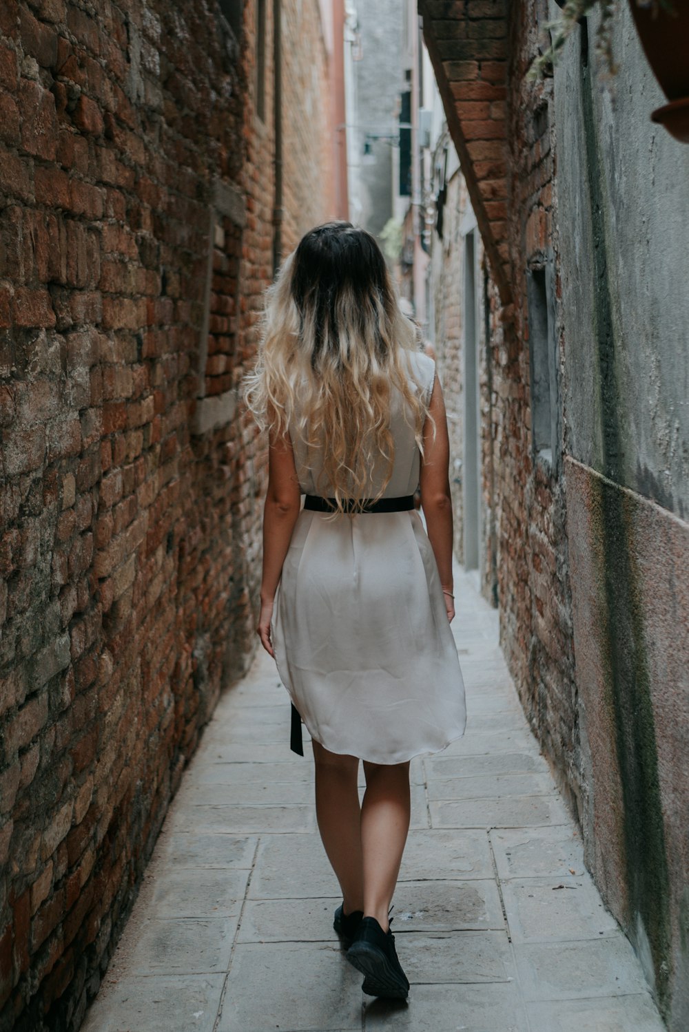 woman in white dress standing on gray concrete brick wall during daytime