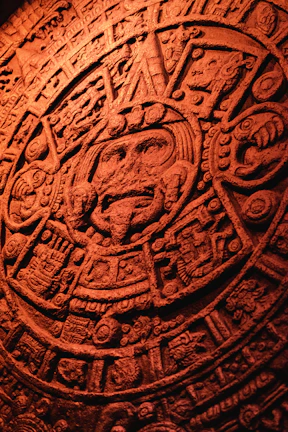 Close-up of a hand-carved stone mask with intricate prehispanic patterns glowing under soft turquoise light.