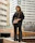 Close-up of a confident woman in a sleek black outfit standing against an urban backdrop