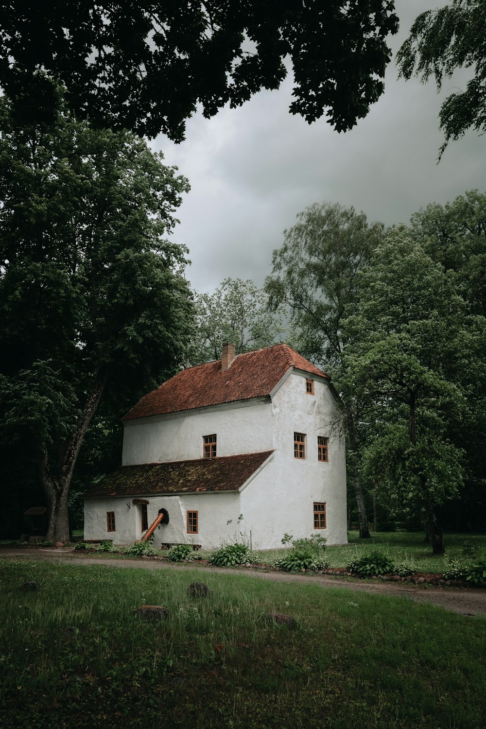 Weißes und braunes Betonhaus in der Nähe von grünen Bäumen unter weißen Wolken tagsüber