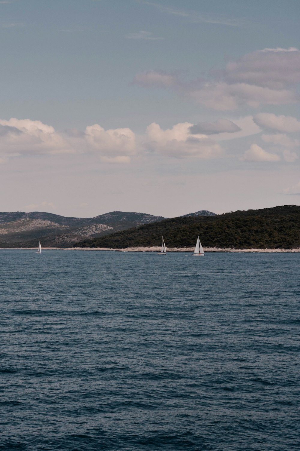 white sailboat on sea under white clouds during daytime